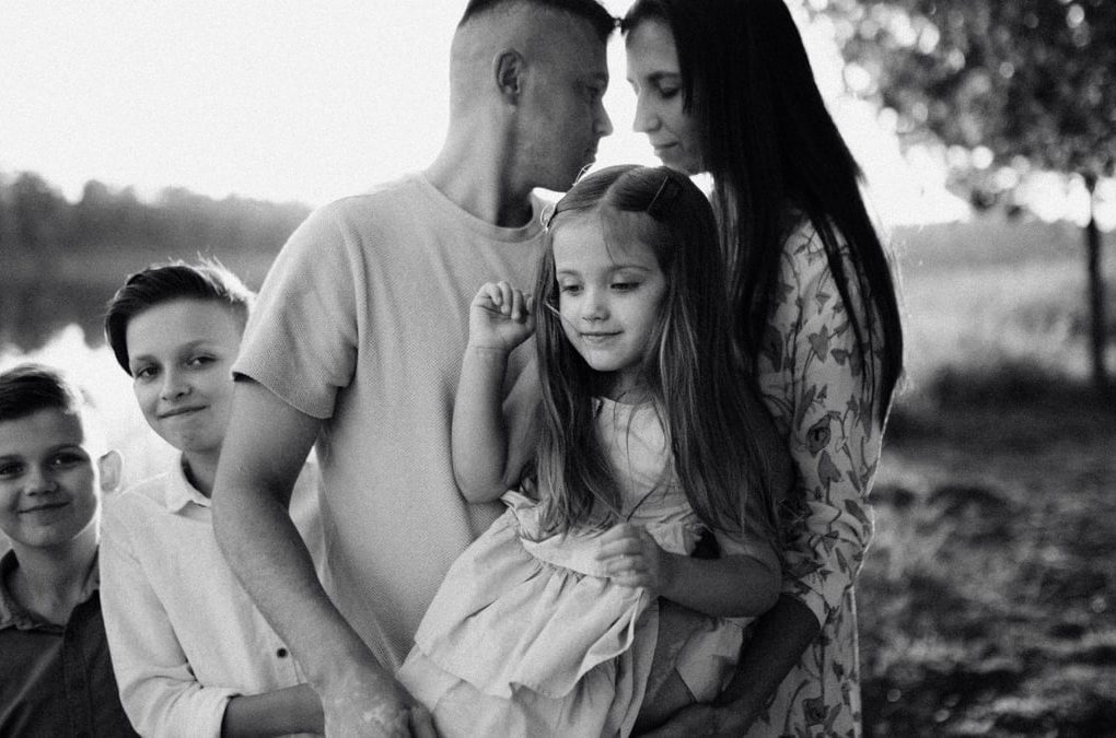 A serene black and white portrait of a family standing by a lake.