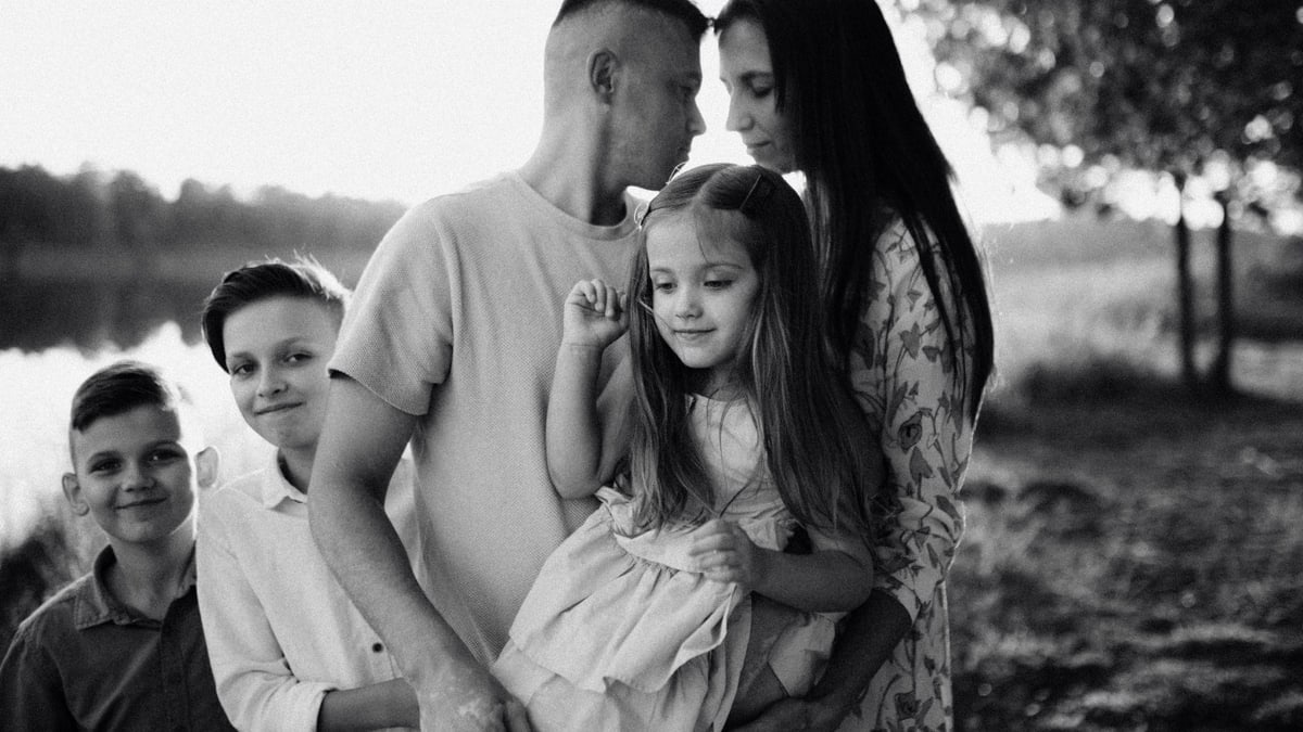 A serene black and white portrait of a family standing by a lake.